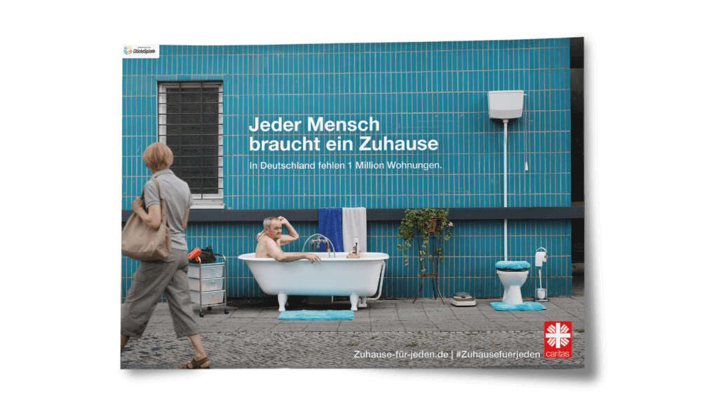 Das Plakat der Kampagne gegen Wohnungsnot für die Caritas von glow zeigt einen älteren Mann in einem auf der Straße aufgestellten Badezimmer. Jeder Mensch braucht ein Zuhause.