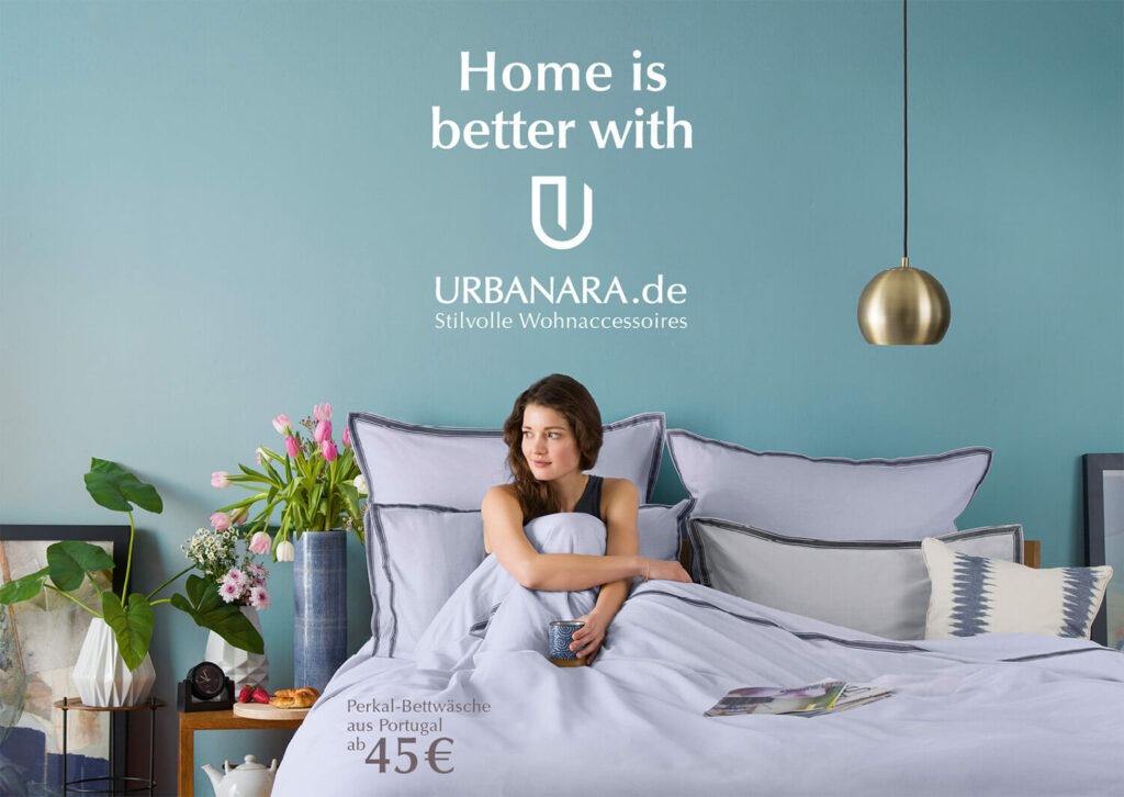 Das Plakat von Urbanara zur Markenkampagne "Home is better with U" zeigt eine Frau unter einer Bettdecke sitzen.